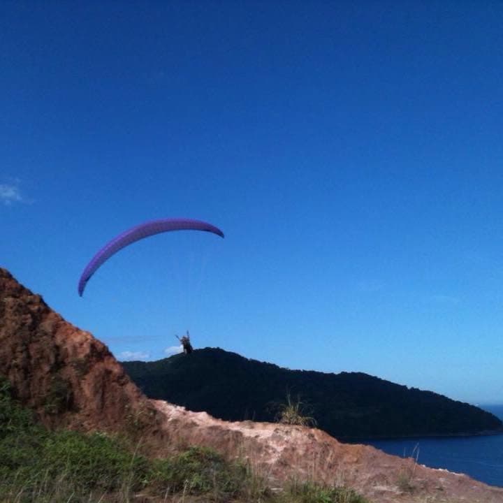 Parapente decolando de um costão, com a mata e o mar ao fundo